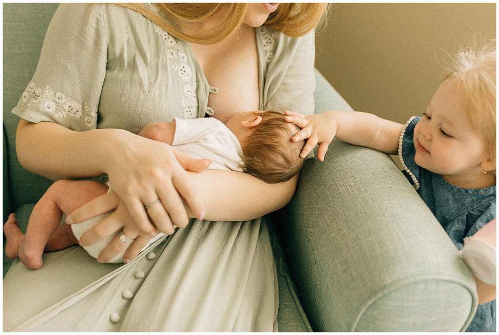 mom holding baby sister touching his head