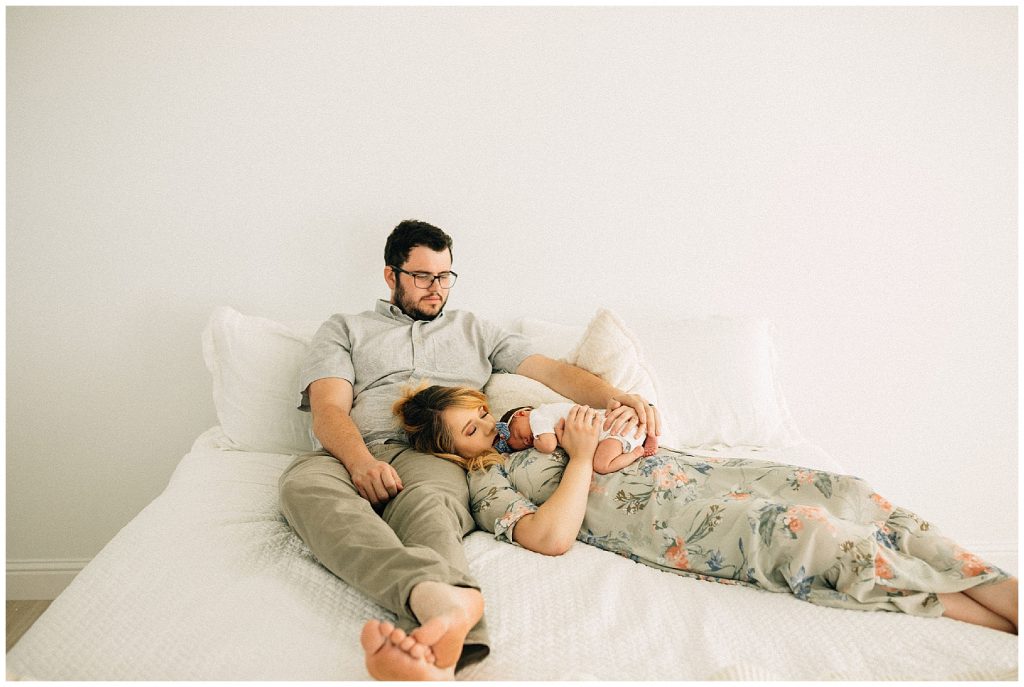 parents holding baby laying on bed